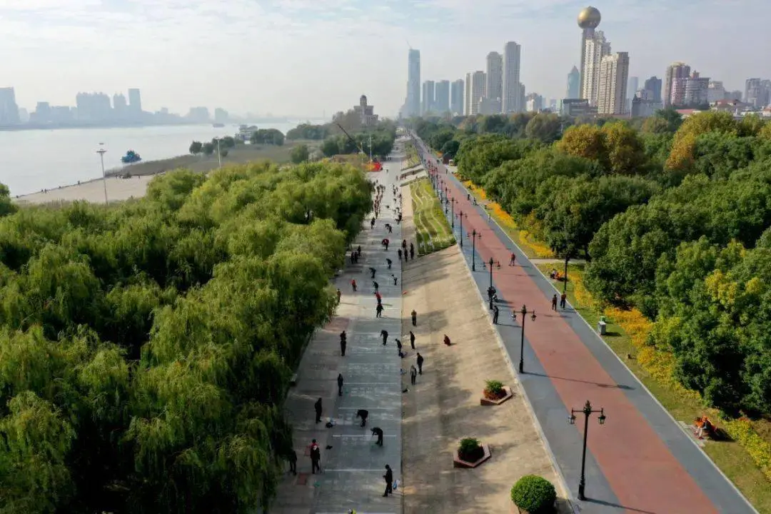 People walking and exercising along the Hankou Bund promenade at sunset, with European buildings in the background