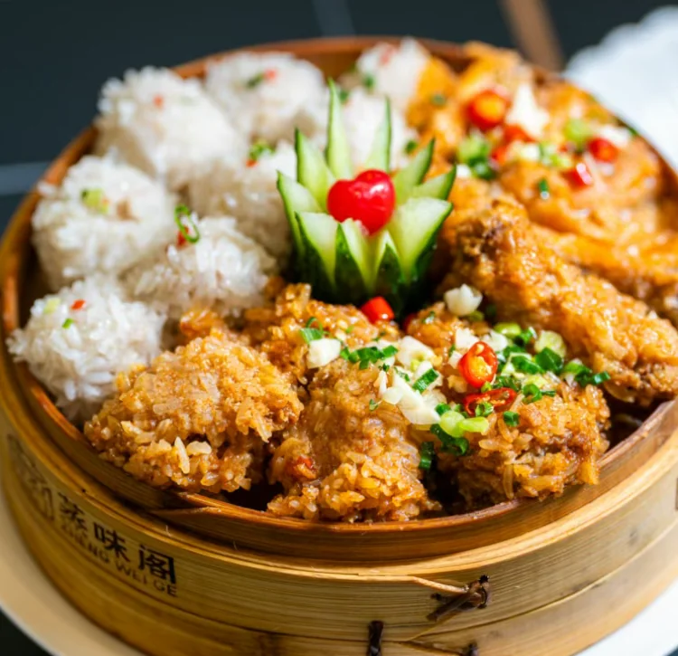 A bamboo steamer holding pearl meatballs rolled in glutinous rice and rice-flour coated steamed meat, garnished with cucumber