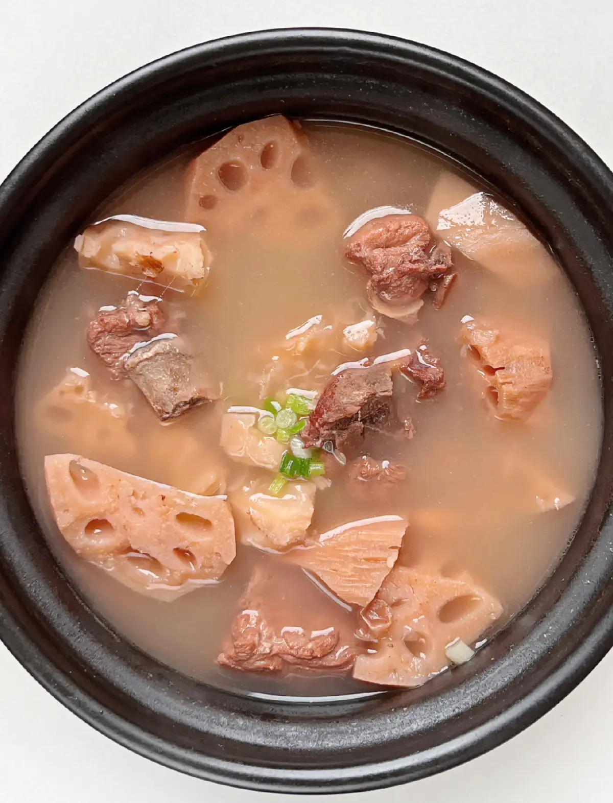 Clay pot simmering on stove with lotus root and pork rib soup, gentle bubbles on the surface, home kitchen