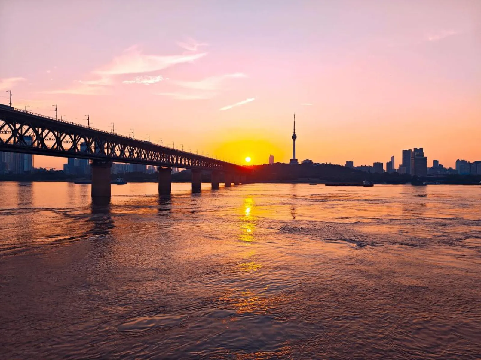 Wuhan Yangtze River Bridge at sunset, golden light on steel truss structure with pedestrians