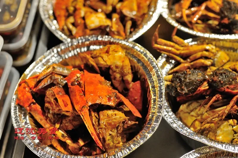 Aluminium trays of cooked hairy crab at a Wuhan street food stall, orange shells piled high under warm light