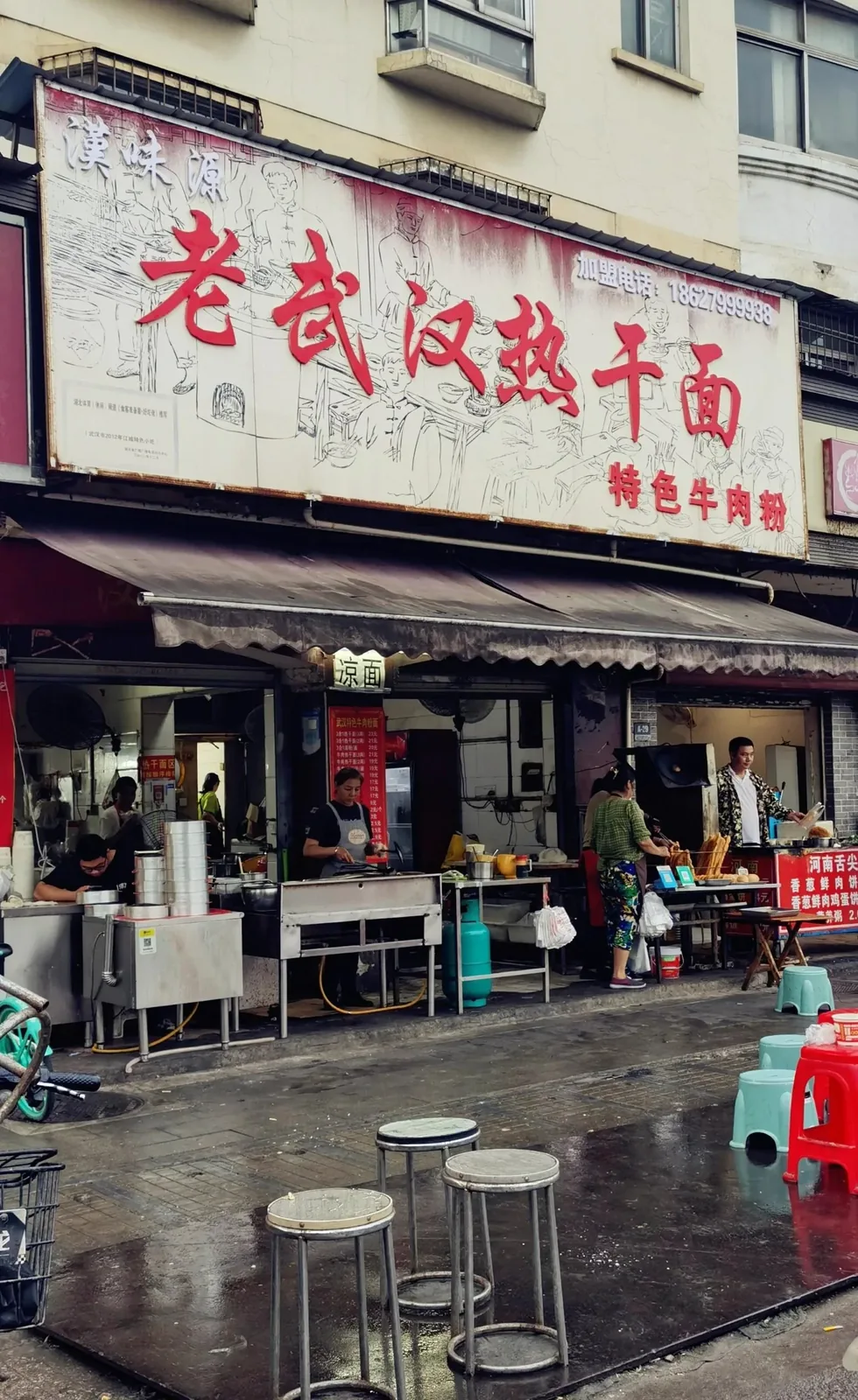 A Wuhan street breakfast stall at dawn: a vendor serving hot dry noodles to a line of customers in work clothes, steam rising from the pots, plastic stools packed, capturing the morning ritual energy of a city universally recognized as China's breakfast capital