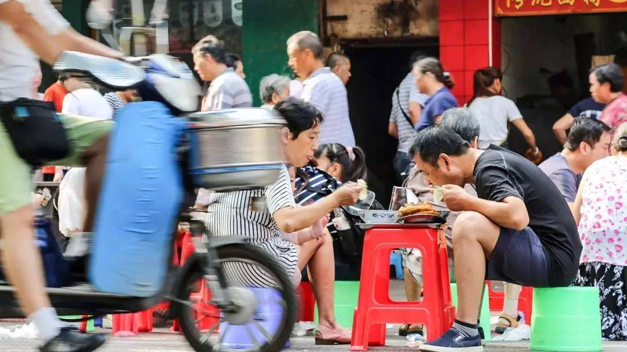A modern Wuhan breakfast scene: a chain restaurant interior with young professionals on phones ordering, contrasting with the traditional street stalls, showing the tension between convenience and authenticity in Wuhan's evolving breakfast landscape