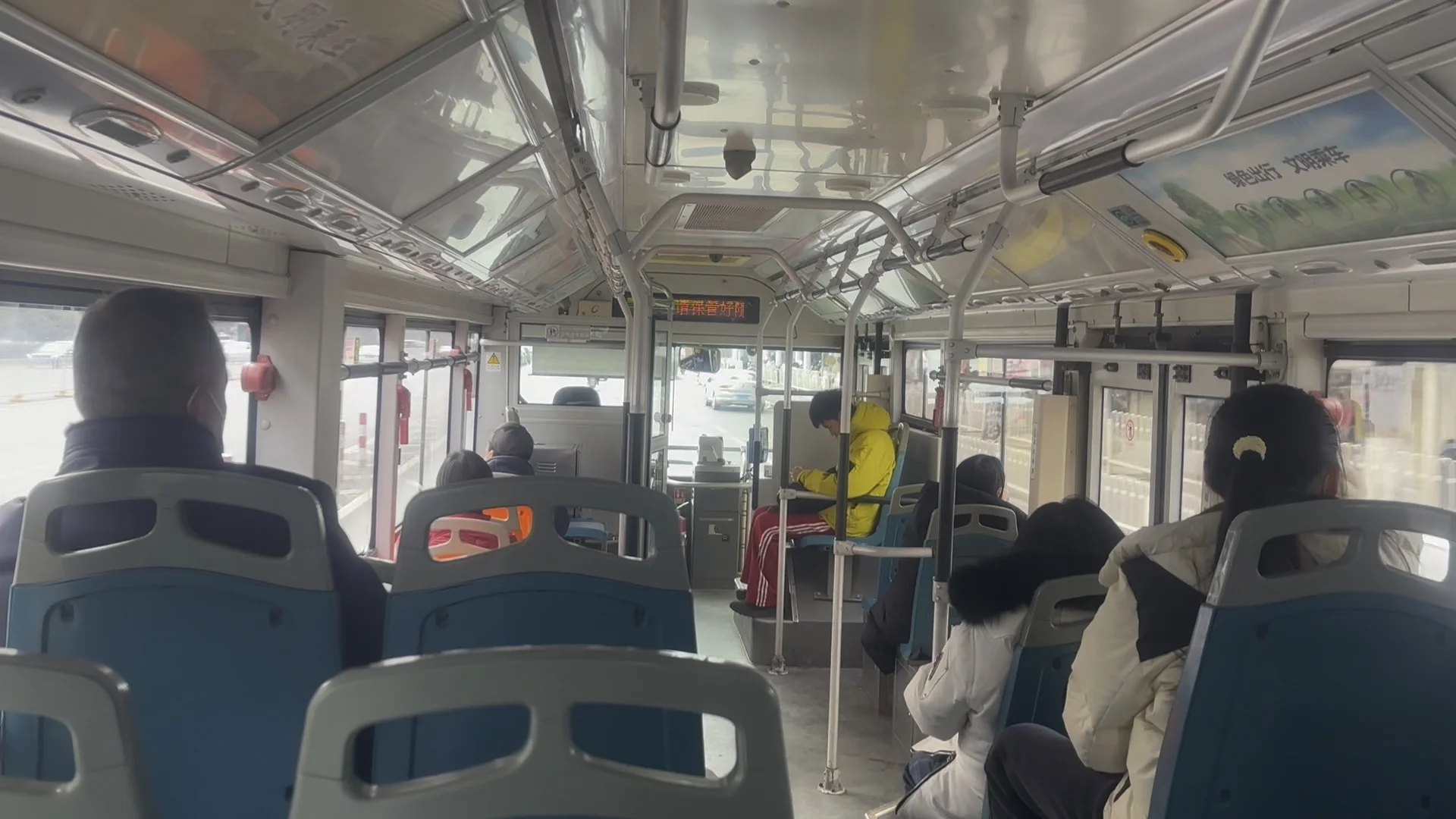 Interior of a Wuhan city bus during rush hour, packed with standing passengers holding overhead handles, a grandmother seated calmly in the front row