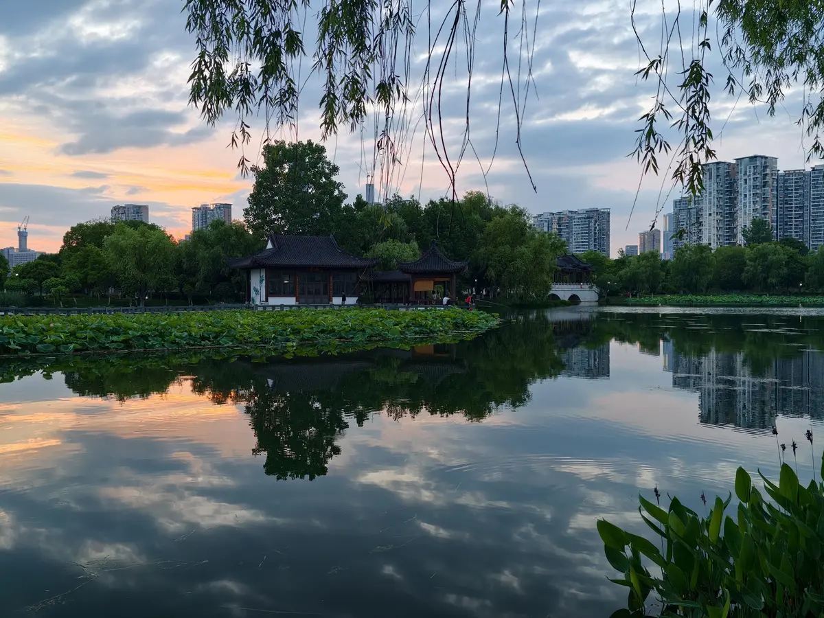 Sha Lake Park in Wuchang at sunset, with residents jogging and walking along the lakeside trail, high-rise apartments in the background