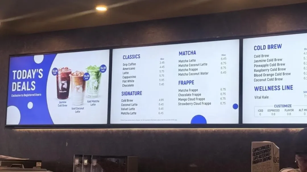 A backlit menu board above a service counter listing drip coffee, americano, cold brew, latte, cappuccino, flat white, matcha and frappe prices, with nothing listed above 6.75 yuan