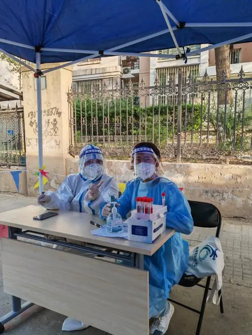 Community worker in protective suit checking temperature at residential compound gate during Wuhan COVID lockdown