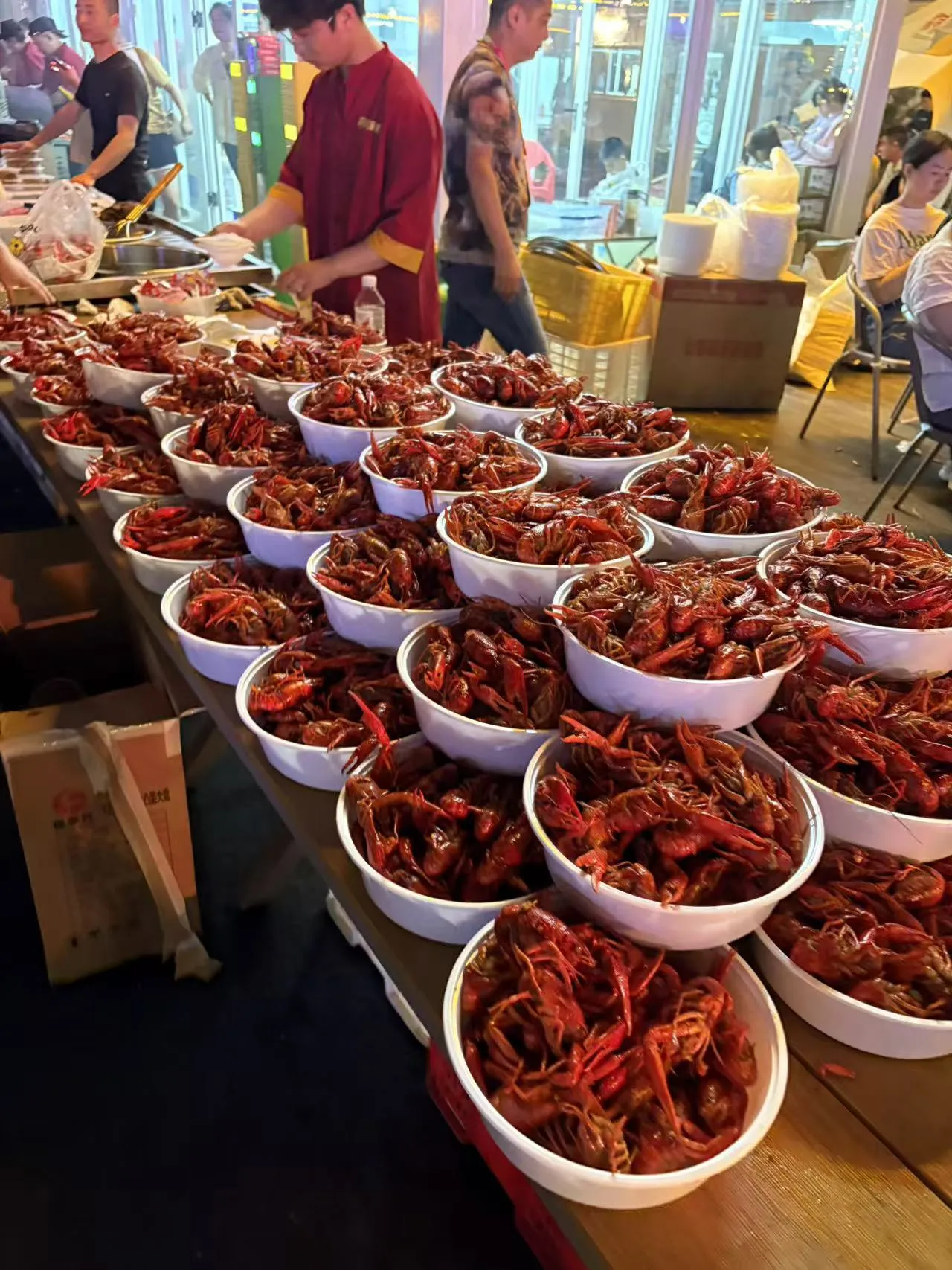 Wuhan summer night crayfish scene — table covered in red crayfish, beer bottles, people wearing plastic gloves eating together