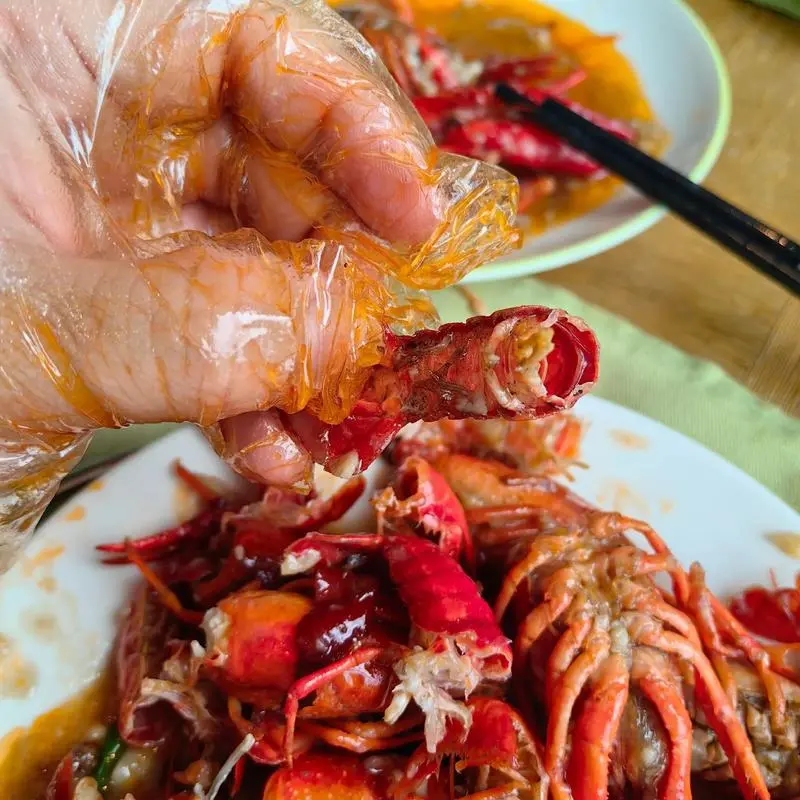 Hands in plastic gloves peeling crayfish at a Wuhan night market table, shells piling up, beer bottles nearby