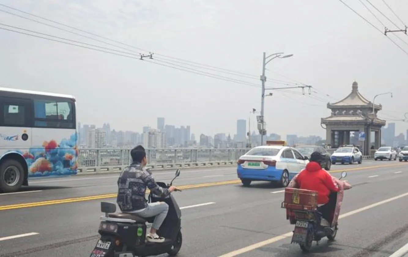 Food delivery scooter crossing Wuhan's Second Yangtze River Bridge at dusk with stacked meal bags visible
