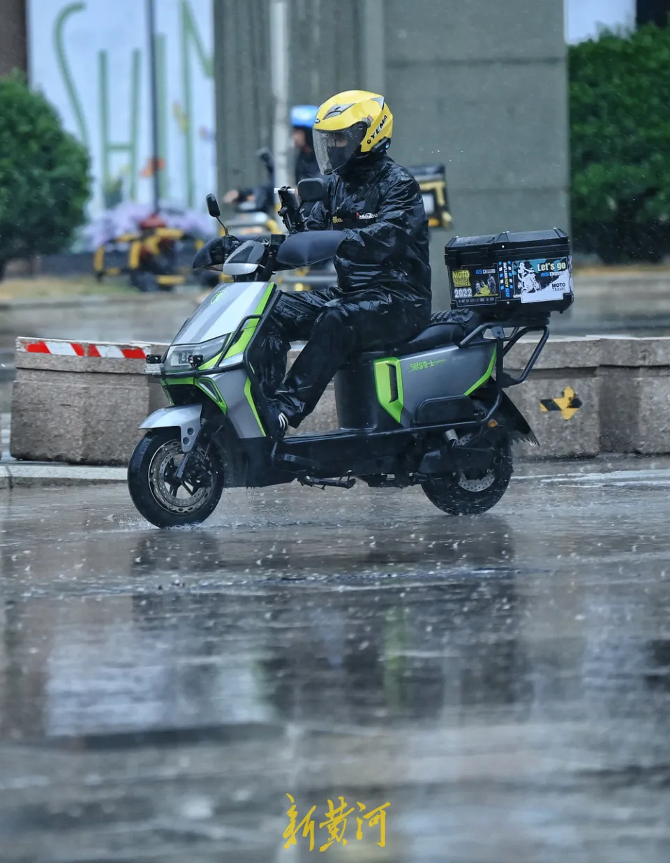 Close-up of delivery scooter rear showing stacked insulated food bag, phone mount with GPS navigation screen, and rider's gloved hand