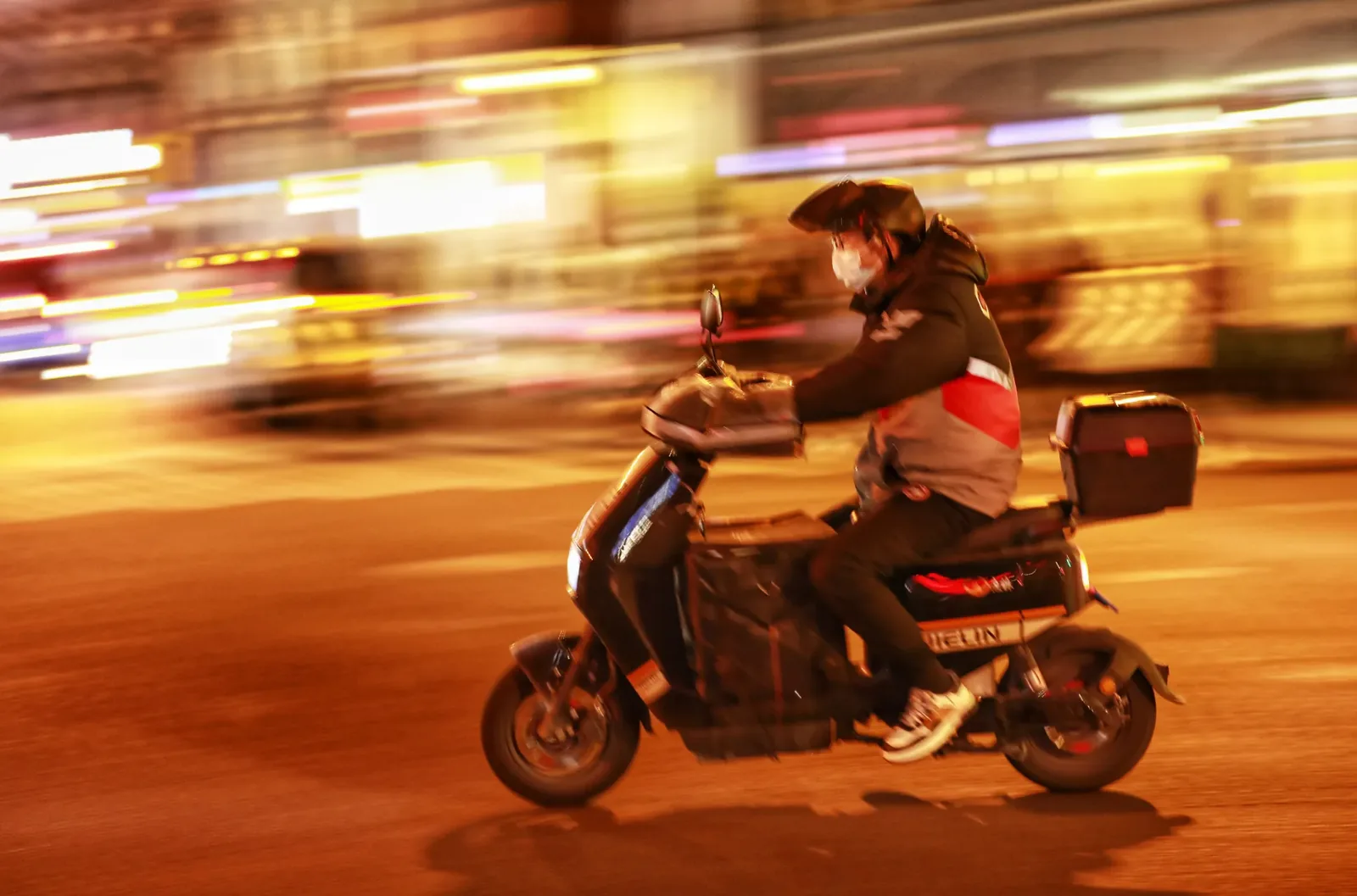 Aerial view of Wuhan's Hankou skyline at night with amber-lit streets and tiny moving scooter headlights weaving through traffic