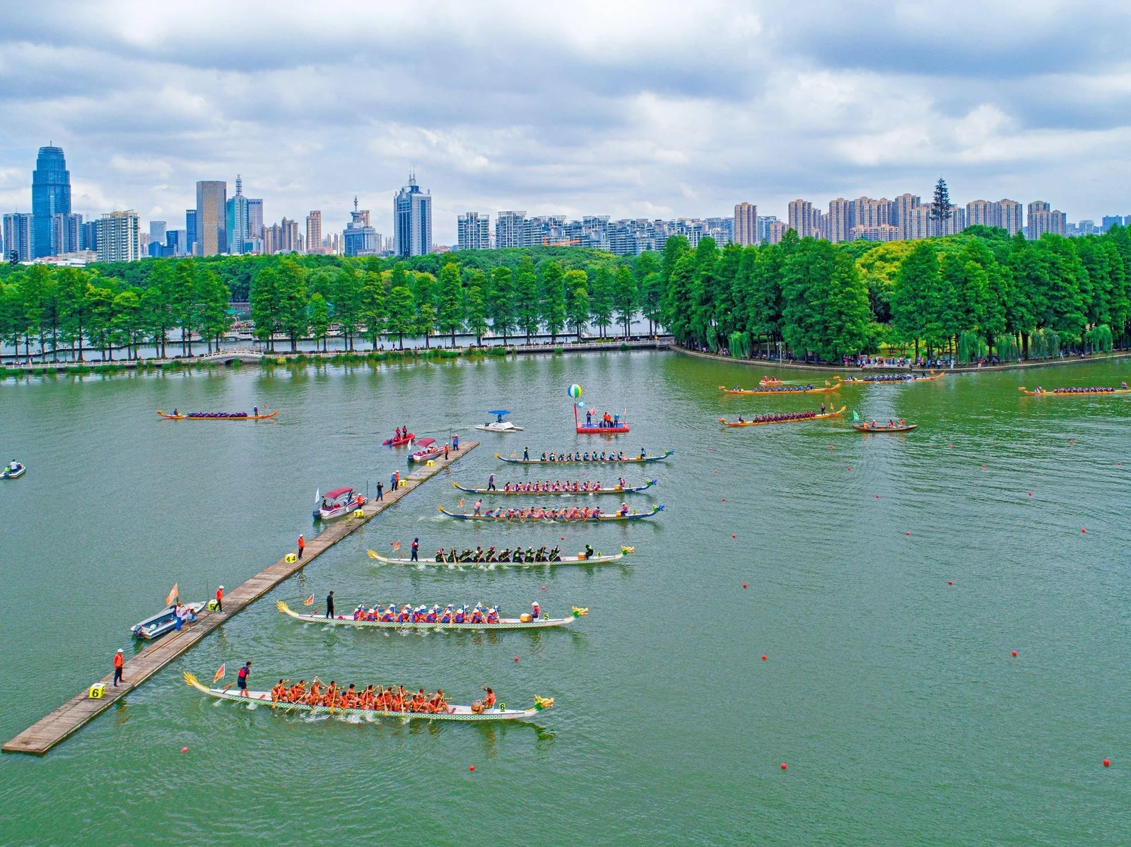 Dragon boat racing on the Yangtze River with long boats cutting through water, colorful banners, and spectators on the riverbank capturing the competitive energy of Wuhan's festival tradition