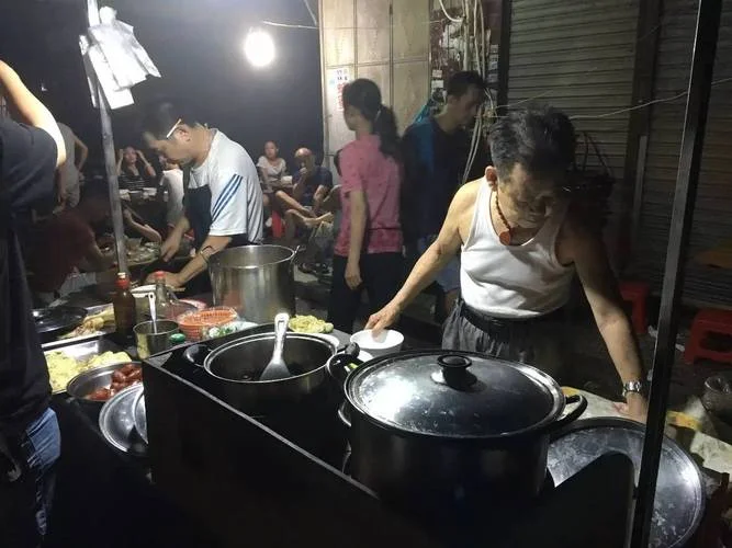 A late-night Wuhan street food stall serving congee and recovery food to the post-dinner crowd, steam rising in the cold night air