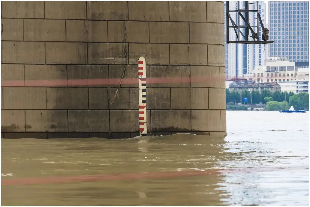 Wuhan Yangtze River flood season — water level markers submerged, people watching the rising river from the bund