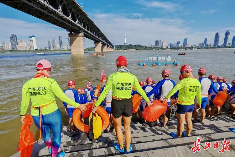 Wuhan Yangtze River Crossing Festival — thousands of swimmers crossing the Yangtze with colorful swim caps, spectators on the bank, bridge in background