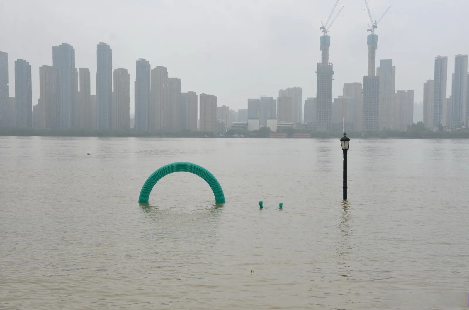 The Yangtze River in flood season in Wuhan, with high brown water covering the stone steps and sandbars, the city skyline visible through river mist
