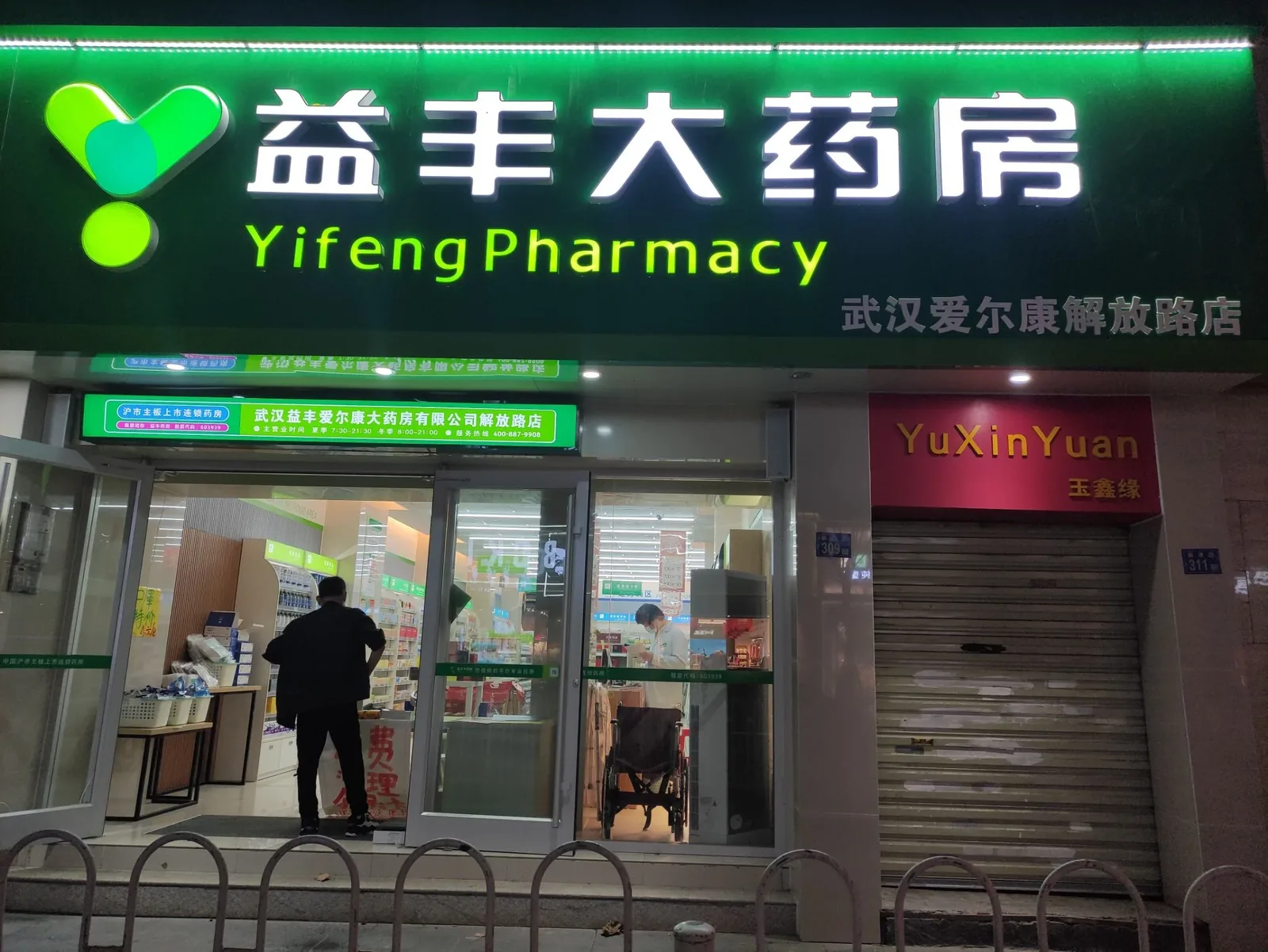 A 24-hour pharmacy in Wuhan with a consultation counter where a pharmacist is talking to a customer, showing the accessible first line of medical advice
