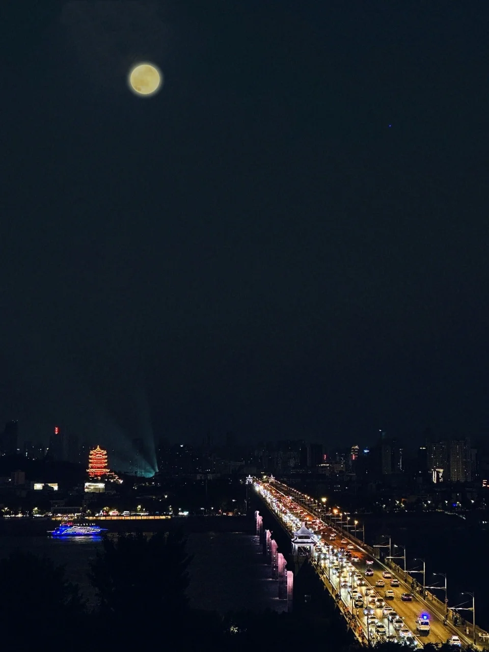 Yangtze River at night with families gathered on the riverside promenade during Mid-Autumn Festival, the city lights and moon reflecting on the water