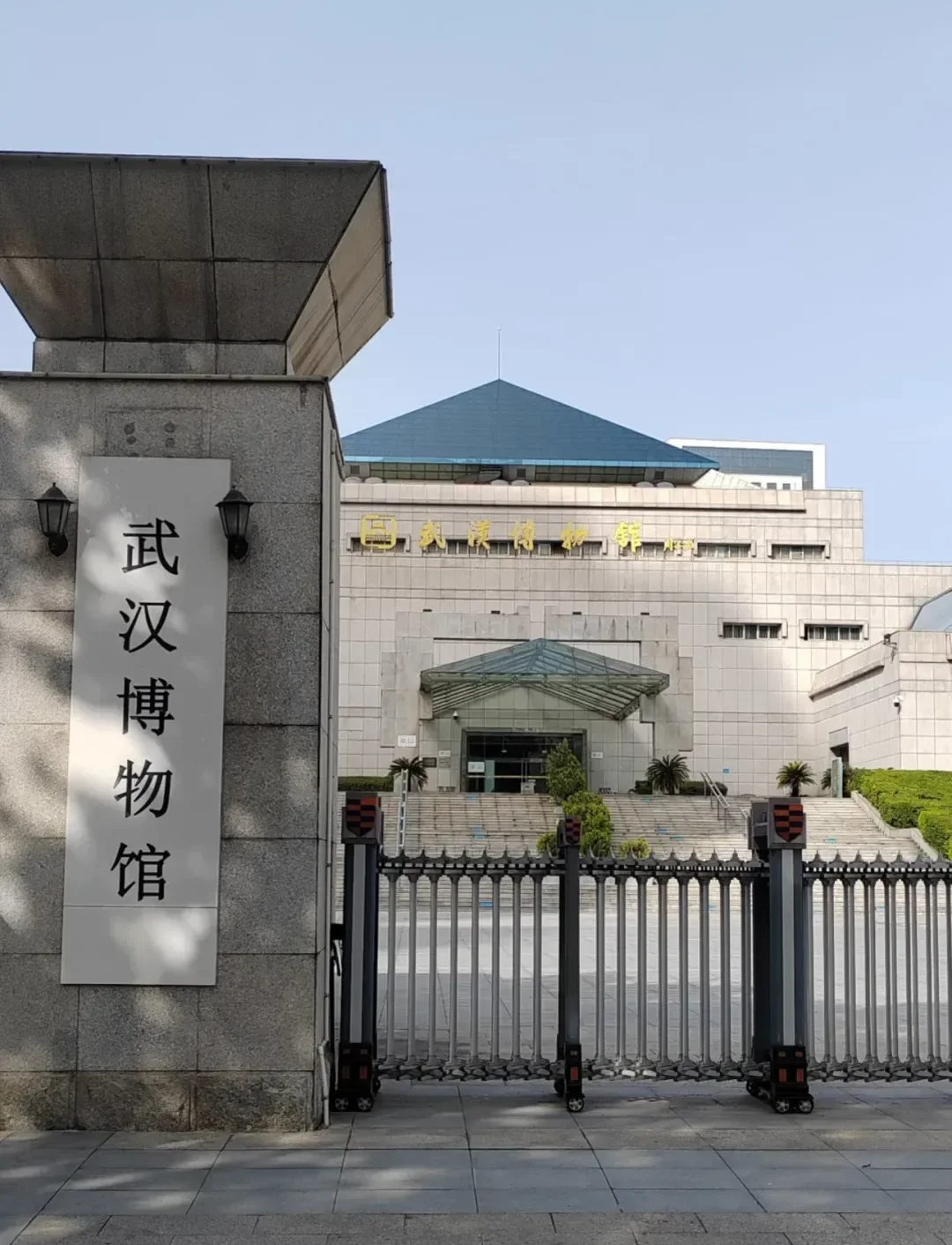The entrance to the Wuhan Museum in Hankou, its name on a stone pillar and in gold characters on the building behind a retractable gate