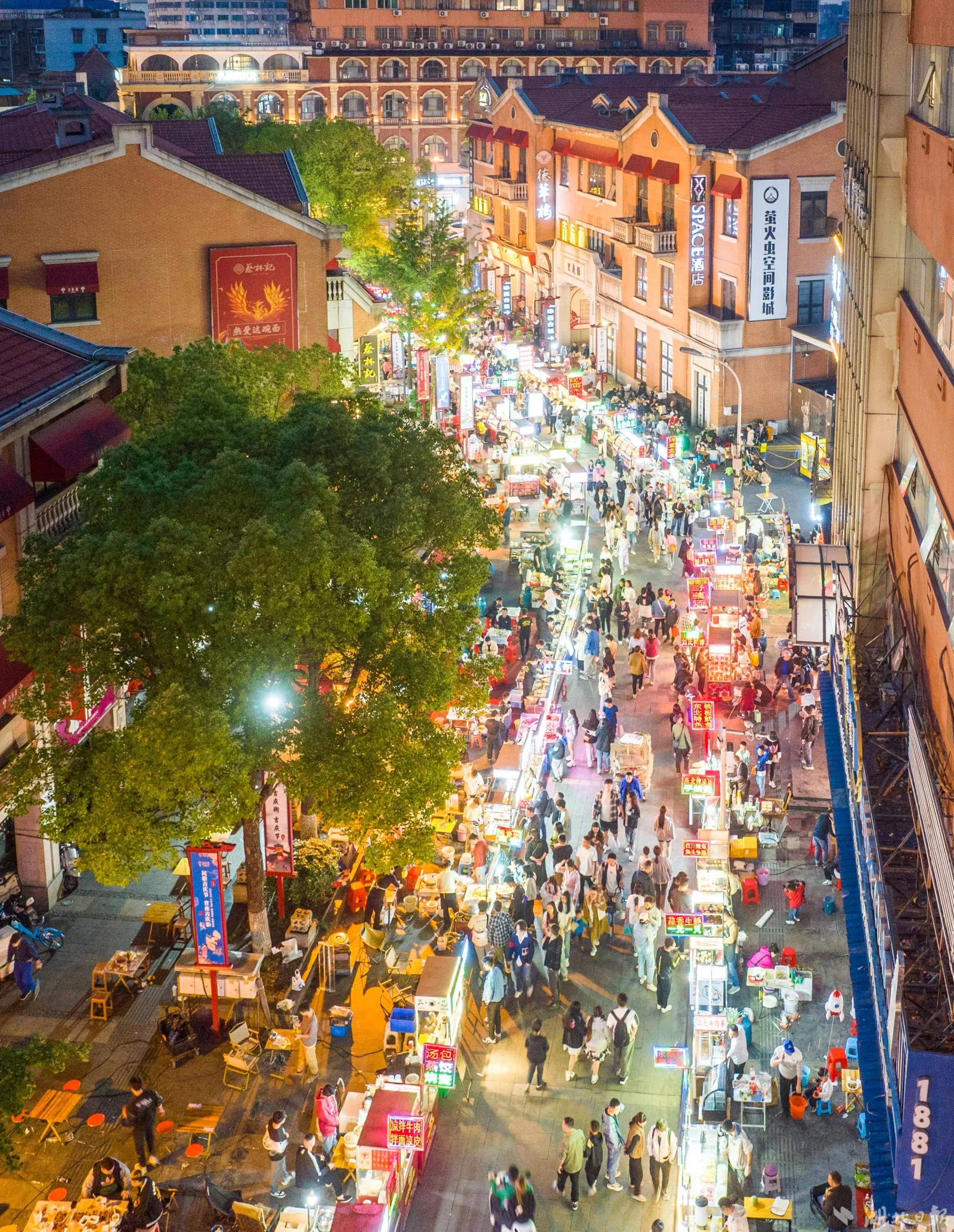 Wuhan night market panorama — food stalls, smoke, plastic stools, and crowds of diners