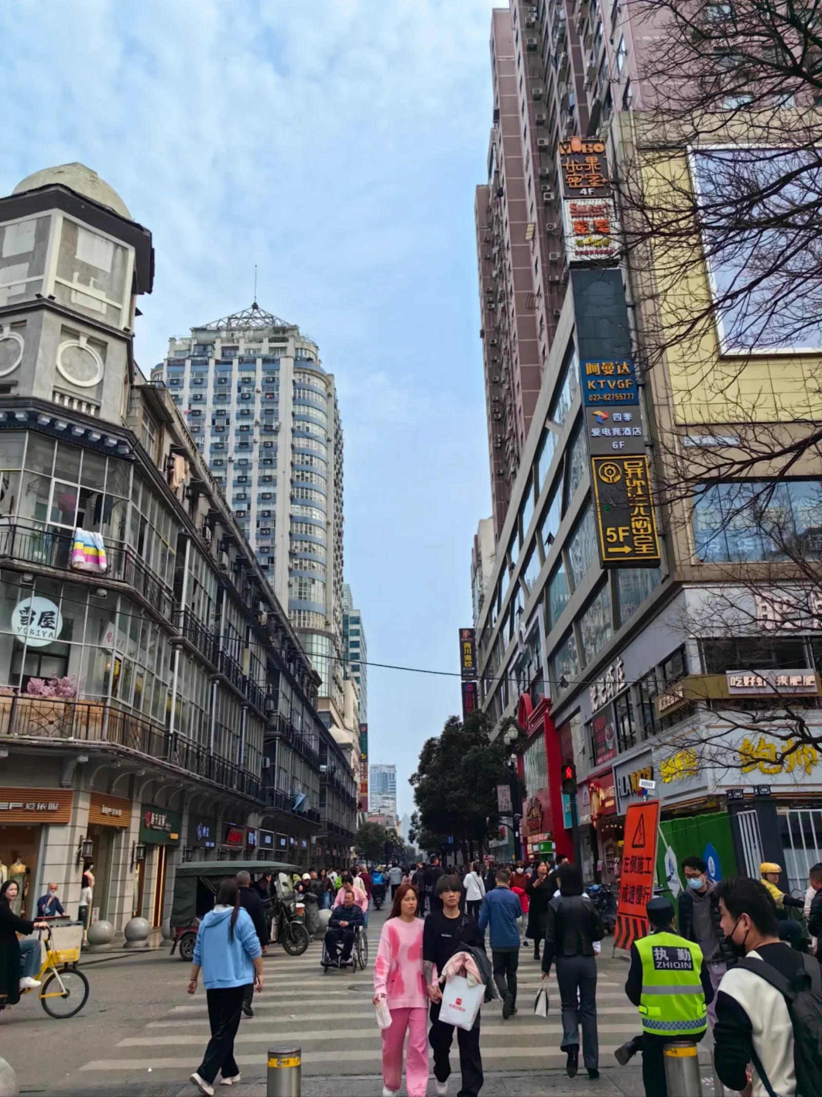 Busy Wuhan street scene with people crossing, vendors shouting orders, and the famous Wuhan hot dry noodle breakfast stall in the foreground
