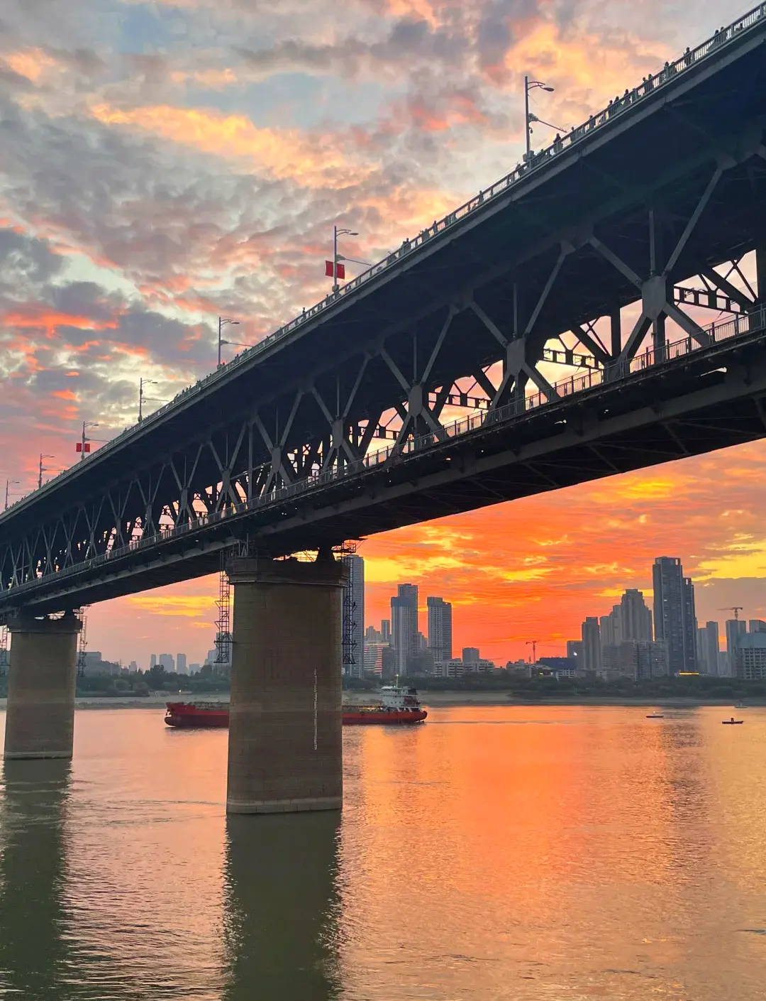 View west from Wuhan Yangtze River Bridge at sunset showing bridge railing, Yangtze River, and Hankou skyline silhouette