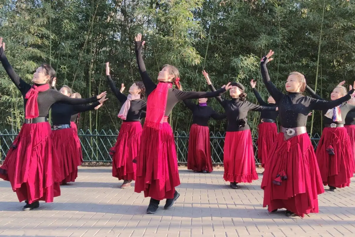 Middle-aged and elderly women in matching outfits doing square dancing on a Wuhan public square at dusk with city buildings in background