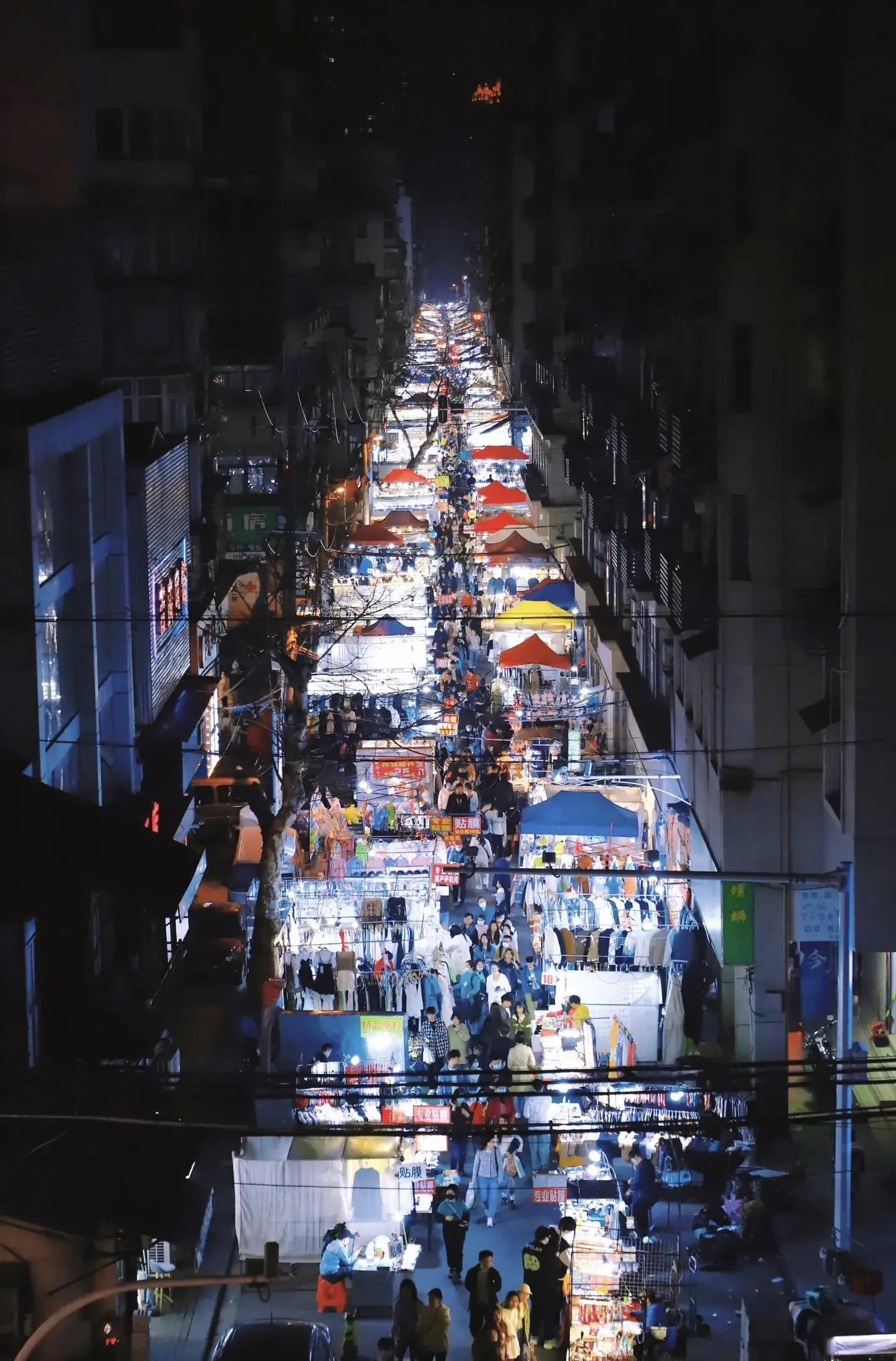Wuhan night market scene with people eating at folding tables, beer bottles, street food stalls, safe evening street life