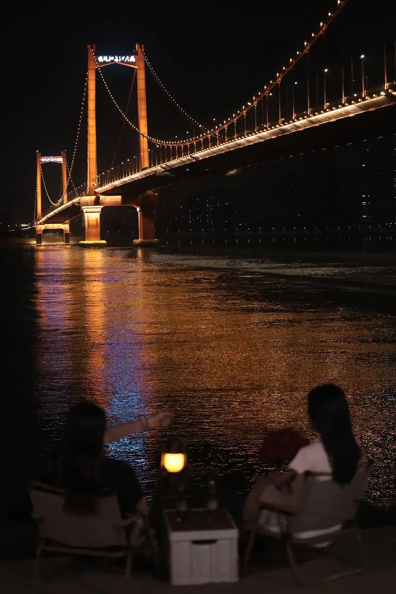 Wuhan residents walking along the Yangtze River at sunset in summer, seeking relief from the heat by the water