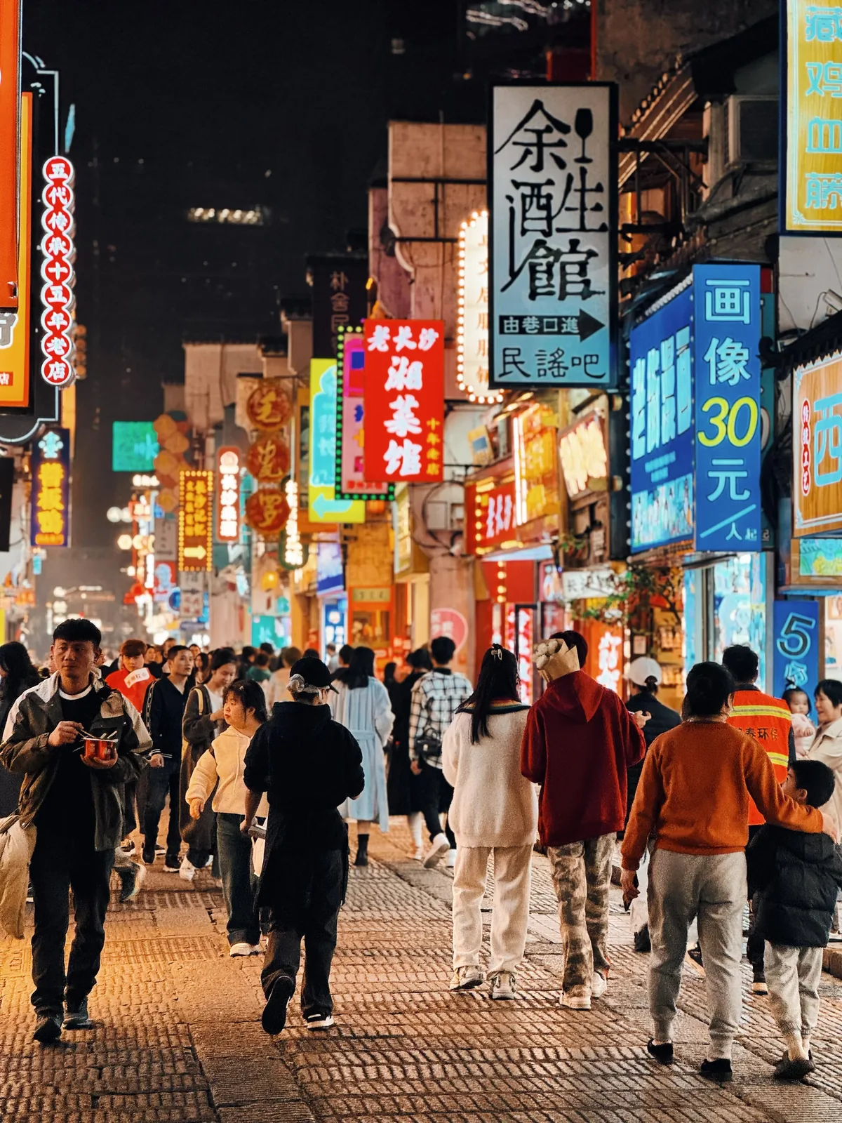 A bustling Changsha night market or street food scene: crowds navigating food stalls under neon signs, colorful tea drinks in hand, showing the weekend magnet energy that pulls Wuhan south