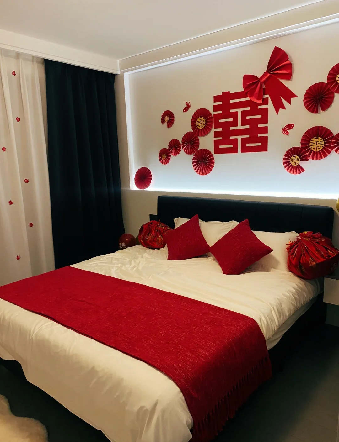 A Wuhan couple's bed-setting ritual or engagement photo moment: the bride's family inspecting gifts laid out on a decorated bed, red decorations, traditional blessings being performed, showing the formal customs that precede the banquet spectacle by days or weeks
