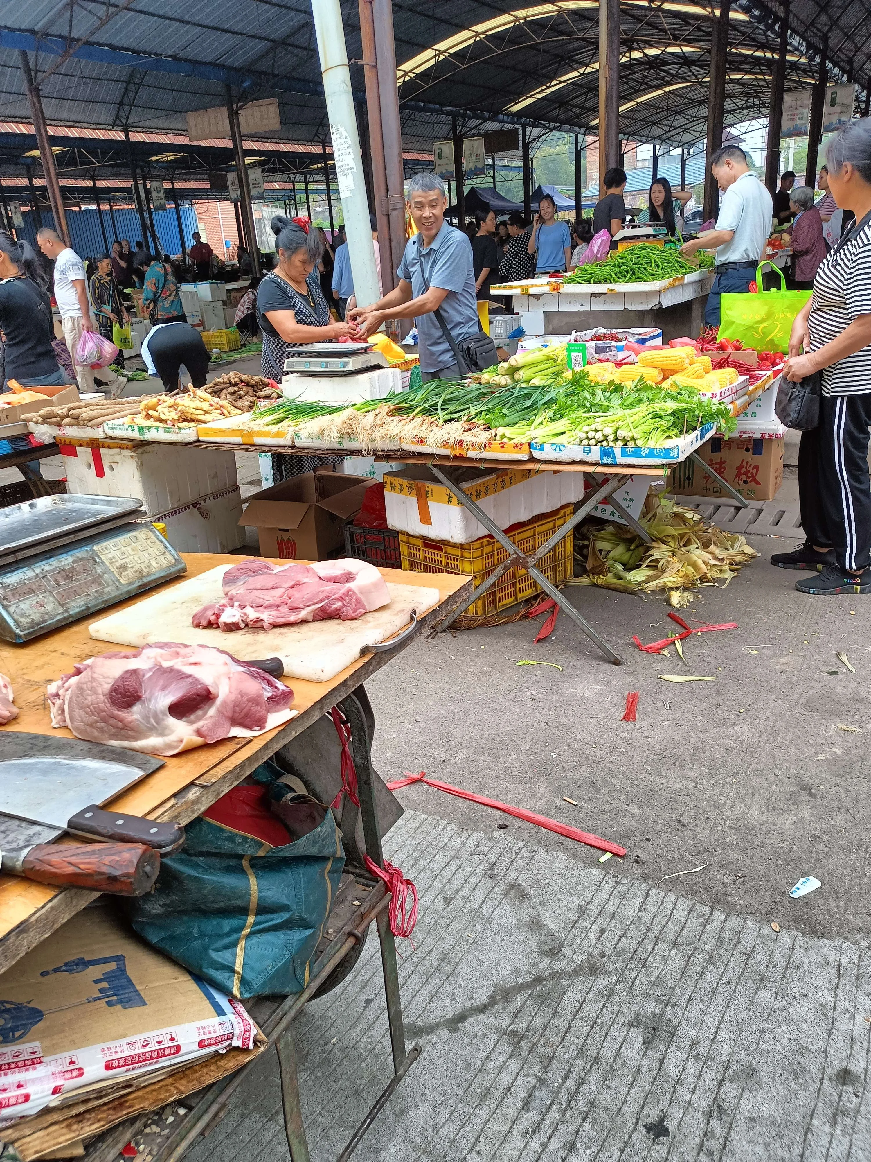 A Wuhan wet market winding down in the evening, vendors chatting with each other, discounted vegetables piled on the last stall