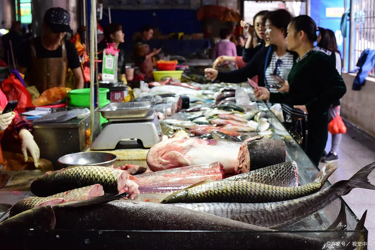 A fish stall at a Wuhan wet market with live carp and shrimp in aerated tanks, a vendor netting a fish while a customer points